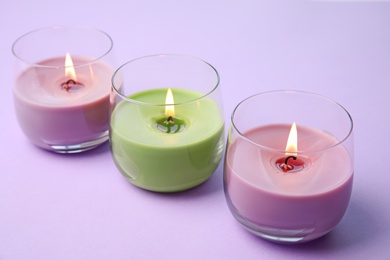 Burning wax candles in glass holders on purple background