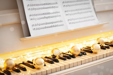 Photo of Golden baubles and fairy lights on piano keys, closeup. Christmas music