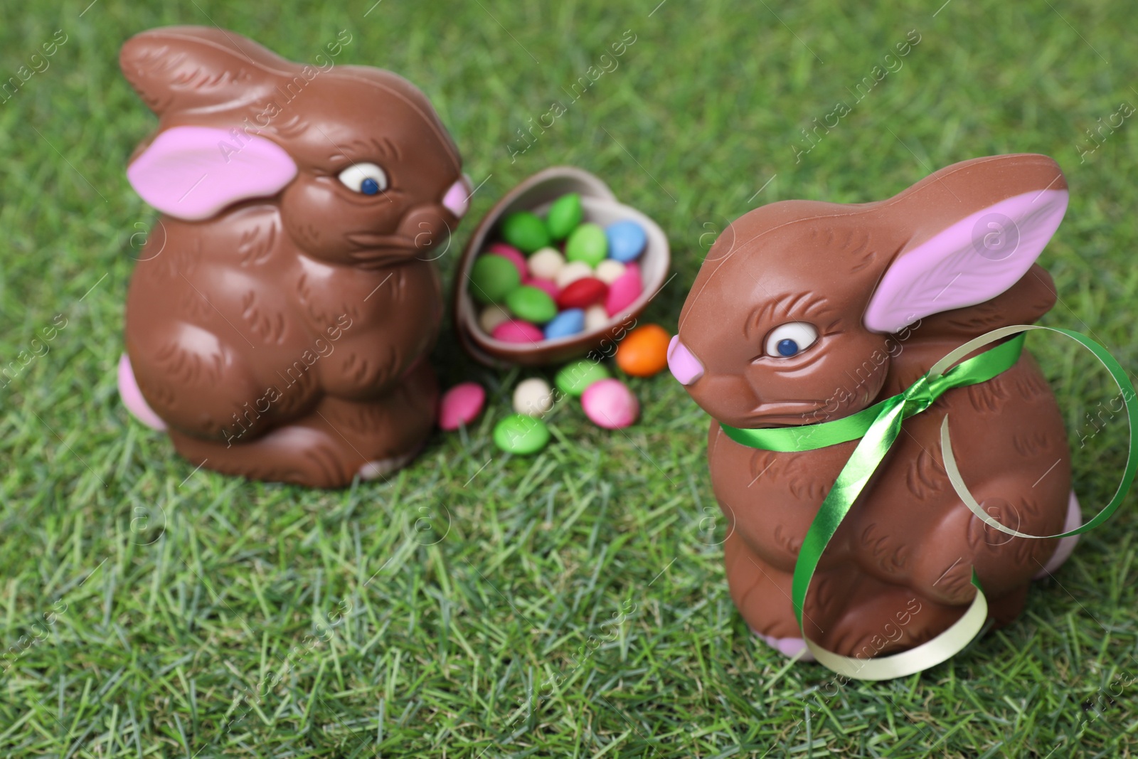 Photo of Easter celebration. Cute chocolate bunnies and egg with colorful candies on green grass