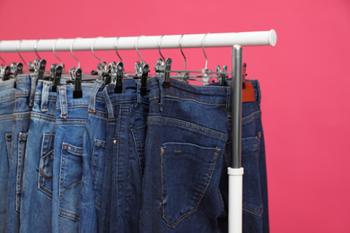 Rack with stylish jeans on pink background, closeup