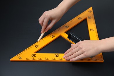 Photo of Woman drawing with chalk and triangle ruler on blackboard, closeup