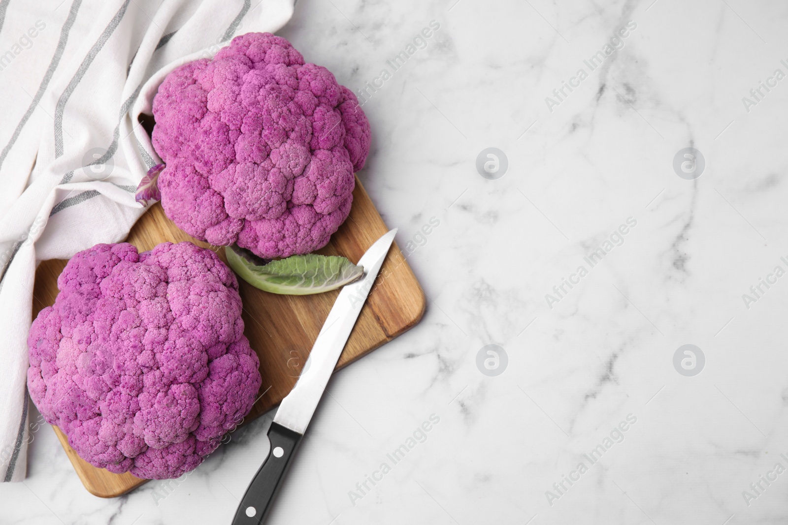 Photo of Fresh cauliflowers, cutting board and knife on white marble table, flat lay. Space for text