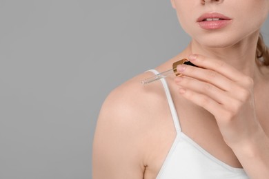 Photo of Woman applying essential oil onto shoulder on grey background, closeup. Space for text