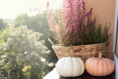 Wicker basket with beautiful heather flowers and pumpkins on windowsill outdoors. Space for text