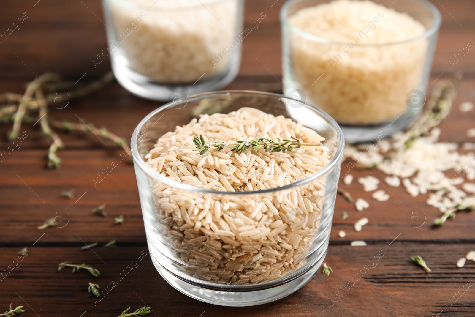 Photo of Glass with raw unpolished rice on wooden table