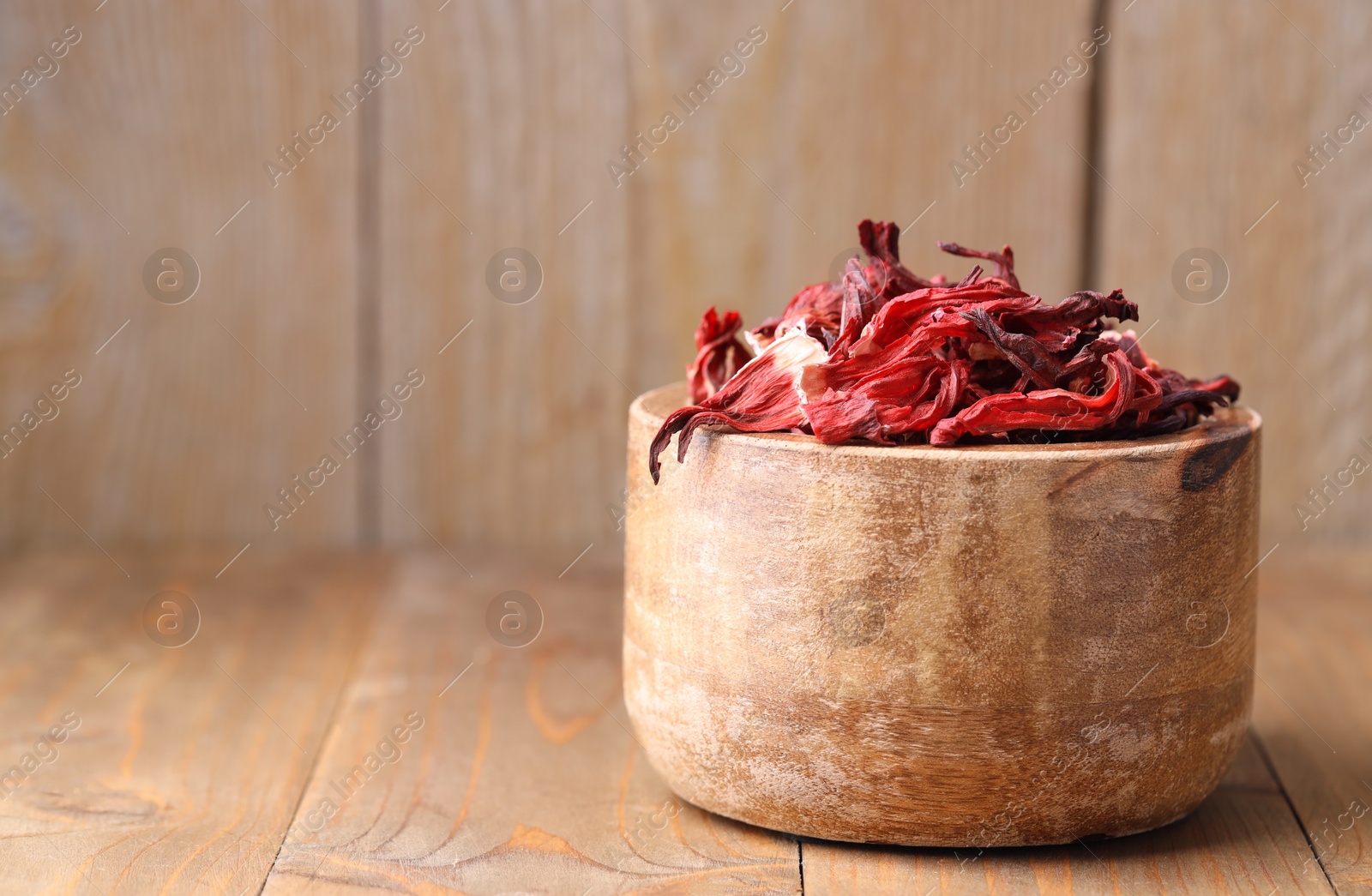 Photo of Dry hibiscus tea in bowl on wooden table, space for text