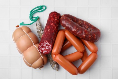 Photo of Different types of sausages on white tiled table, flat lay