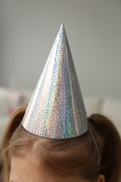 Photo of Little girl wearing party hat at home, closeup