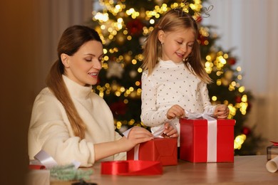 Photo of Christmas presents wrapping. Mother and her little daughter decorating gift boxes with ribbon at home