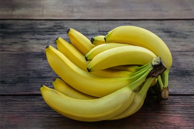 Photo of Bunches of ripe yellow bananas on wooden table