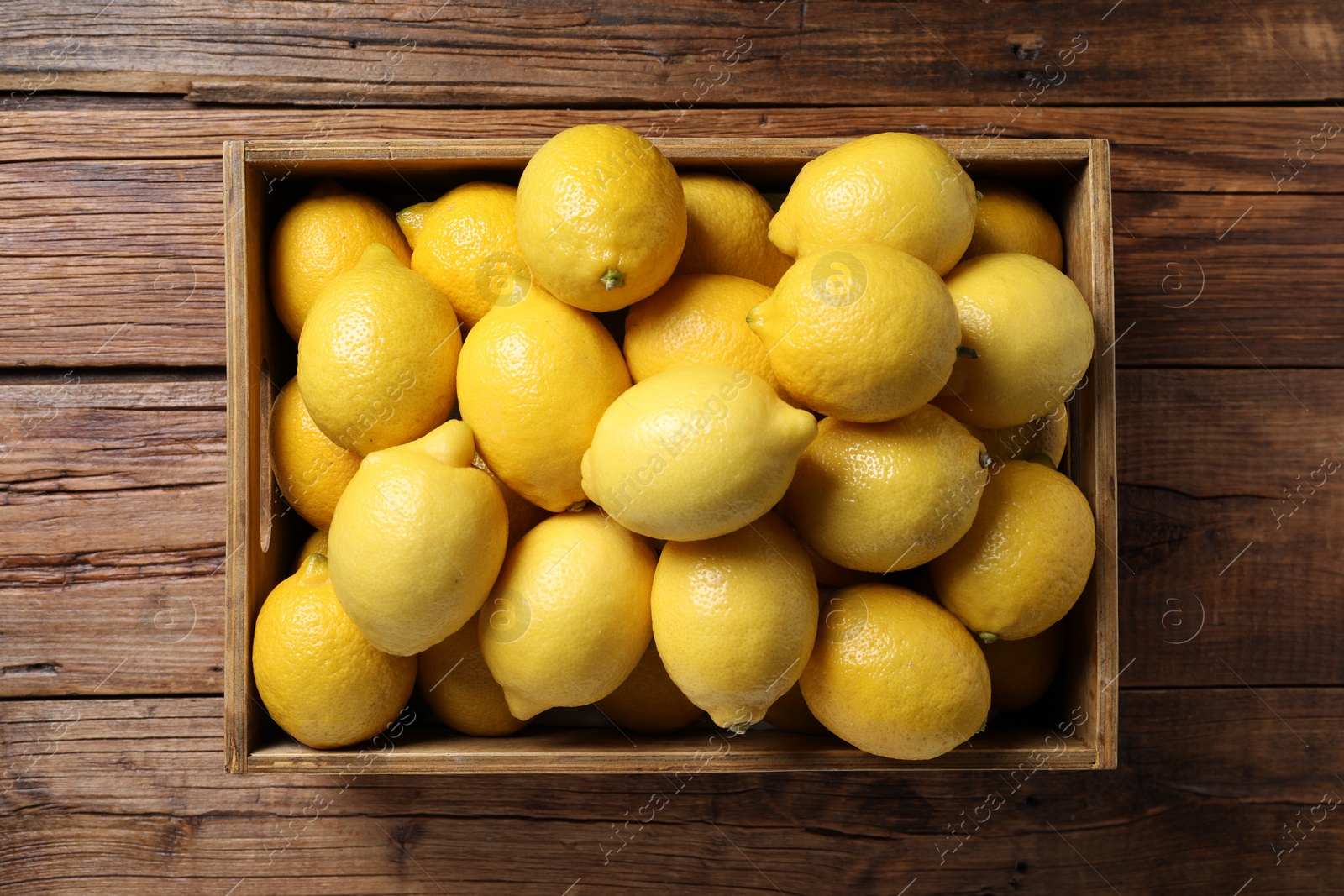 Photo of Fresh lemons in crate on wooden table, top view