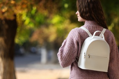 Photo of Young woman with stylish white backpack in park, back view. Space for text