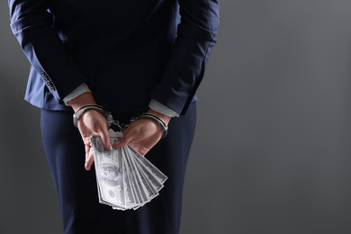 Woman in handcuffs holding bribe money on dark background, closeup. Space for text