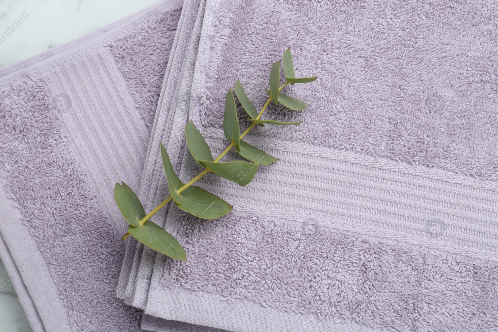 Photo of Violet terry towels and eucalyptus branch on white table, top view
