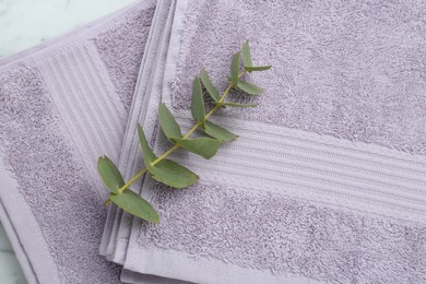 Violet terry towels and eucalyptus branch on white table, top view