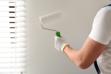 Photo of Man painting wall with white dye indoors, closeup