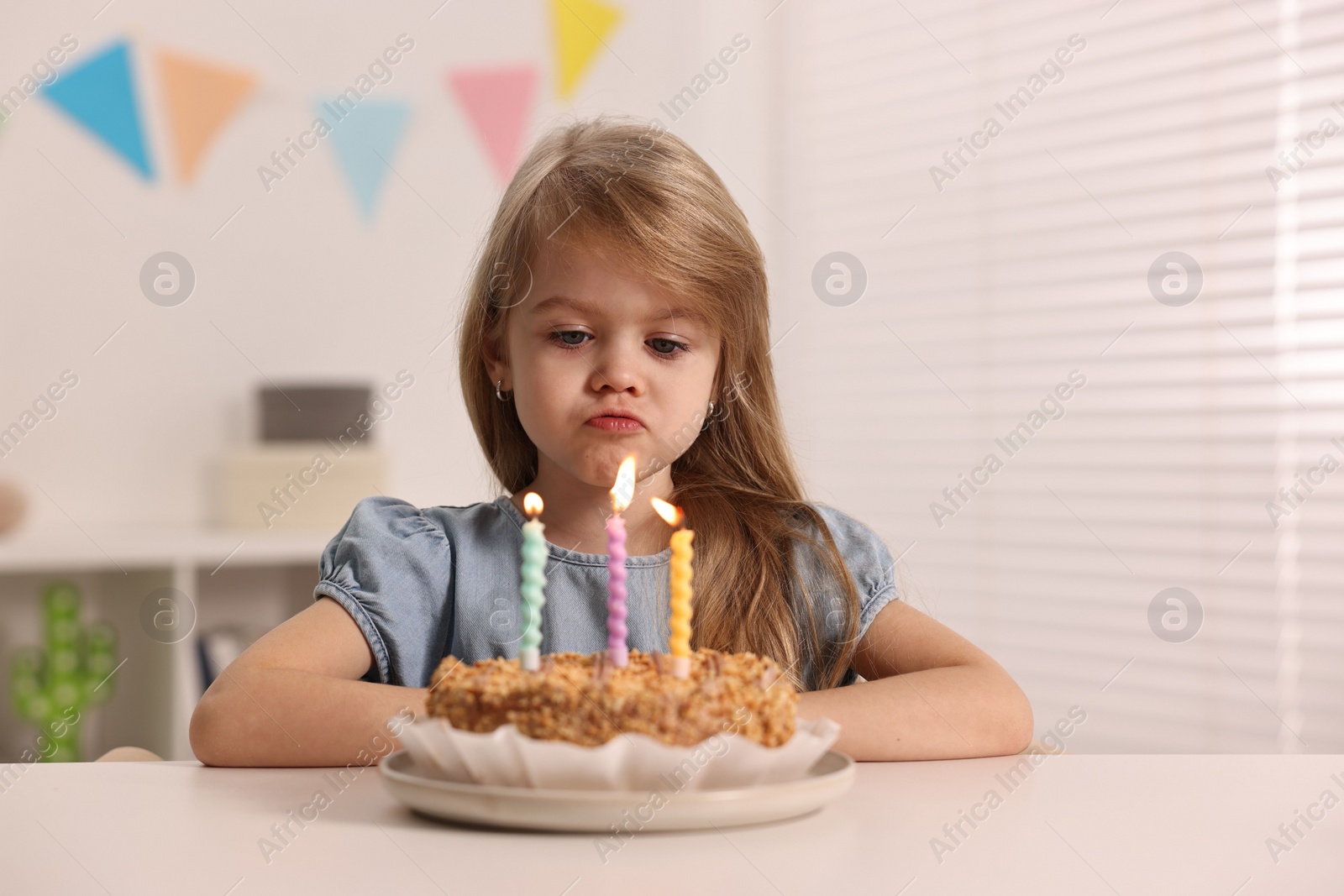 Photo of Cute girl with birthday cake at table indoors