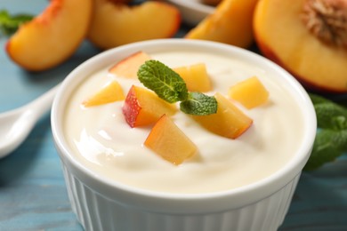 Photo of Delicious yogurt with fresh peach and mint on light blue table, closeup