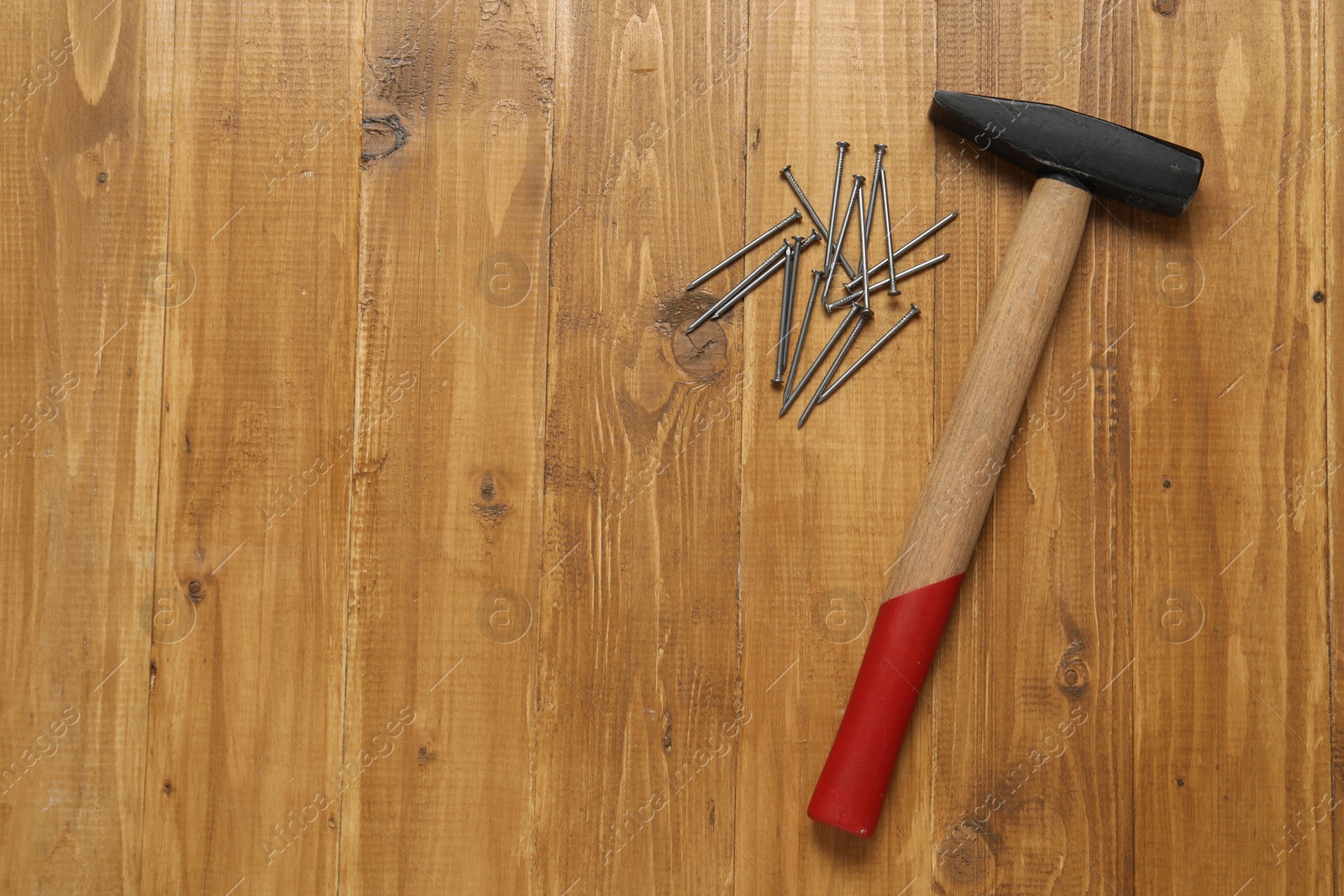 Photo of New hammer and metal nails on wooden table, flat lay. Space for text