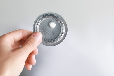 Photo of Woman holding blister of emergency contraception pill against blurred background, closeup. Space for text