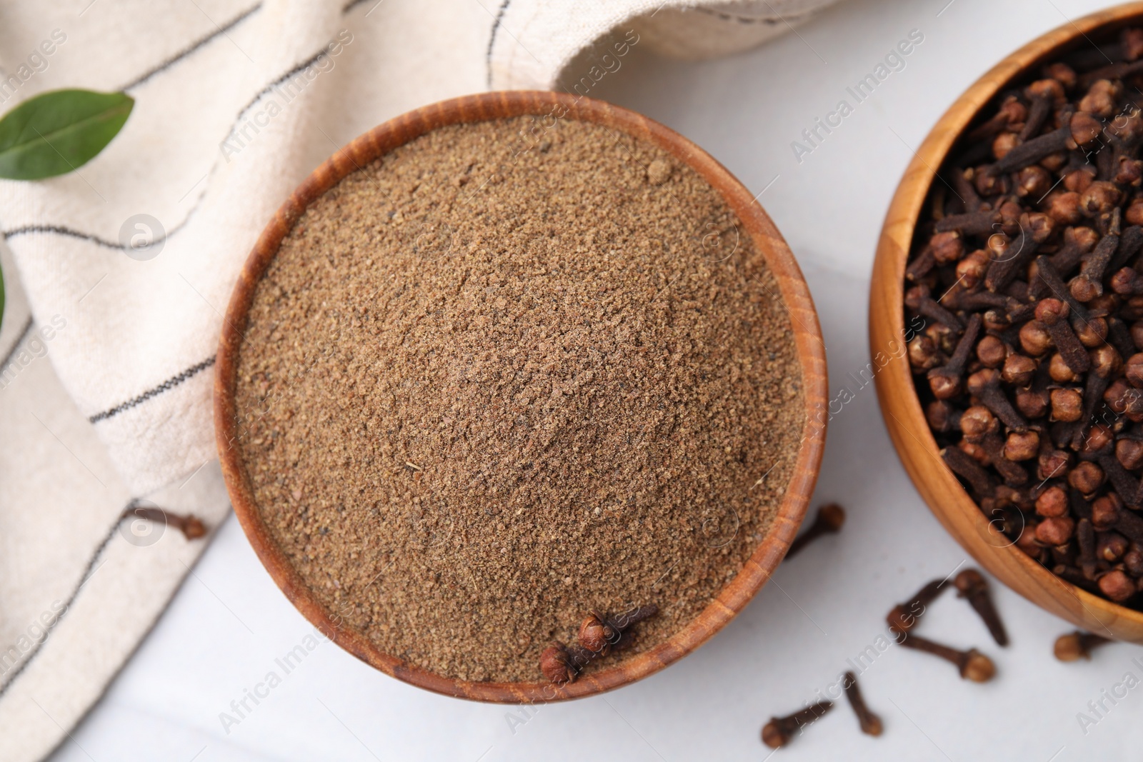 Photo of Aromatic clove powder and dried buds in bowls on white table, flat lay