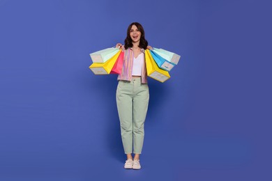 Beautiful young woman with paper shopping bags on purple background