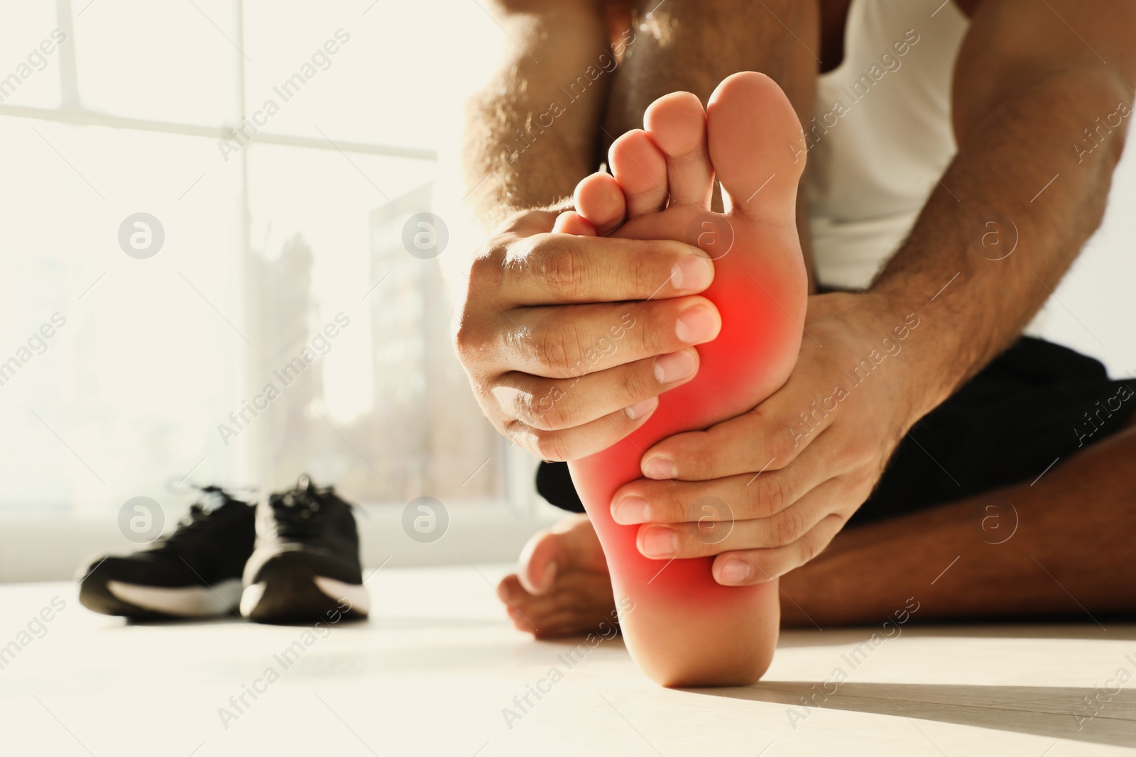 Image of Man suffering from foot pain on floor indoors, closeup