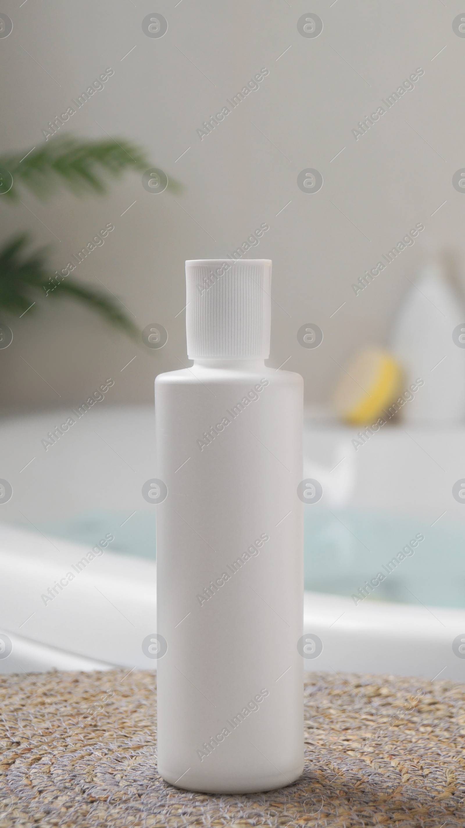 Photo of White bottle of bubble bath on wicker mat near tub indoors