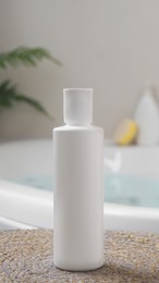 Photo of White bottle of bubble bath on wicker mat near tub indoors
