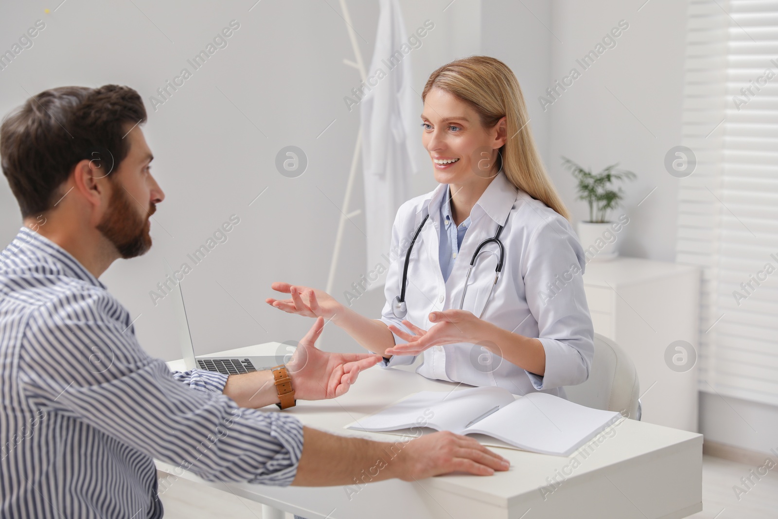 Photo of Happy doctor consulting patient at white table in clinic