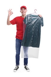 Dry-cleaning delivery. Happy courier holding dress in plastic bag and showing OK gesture on white background