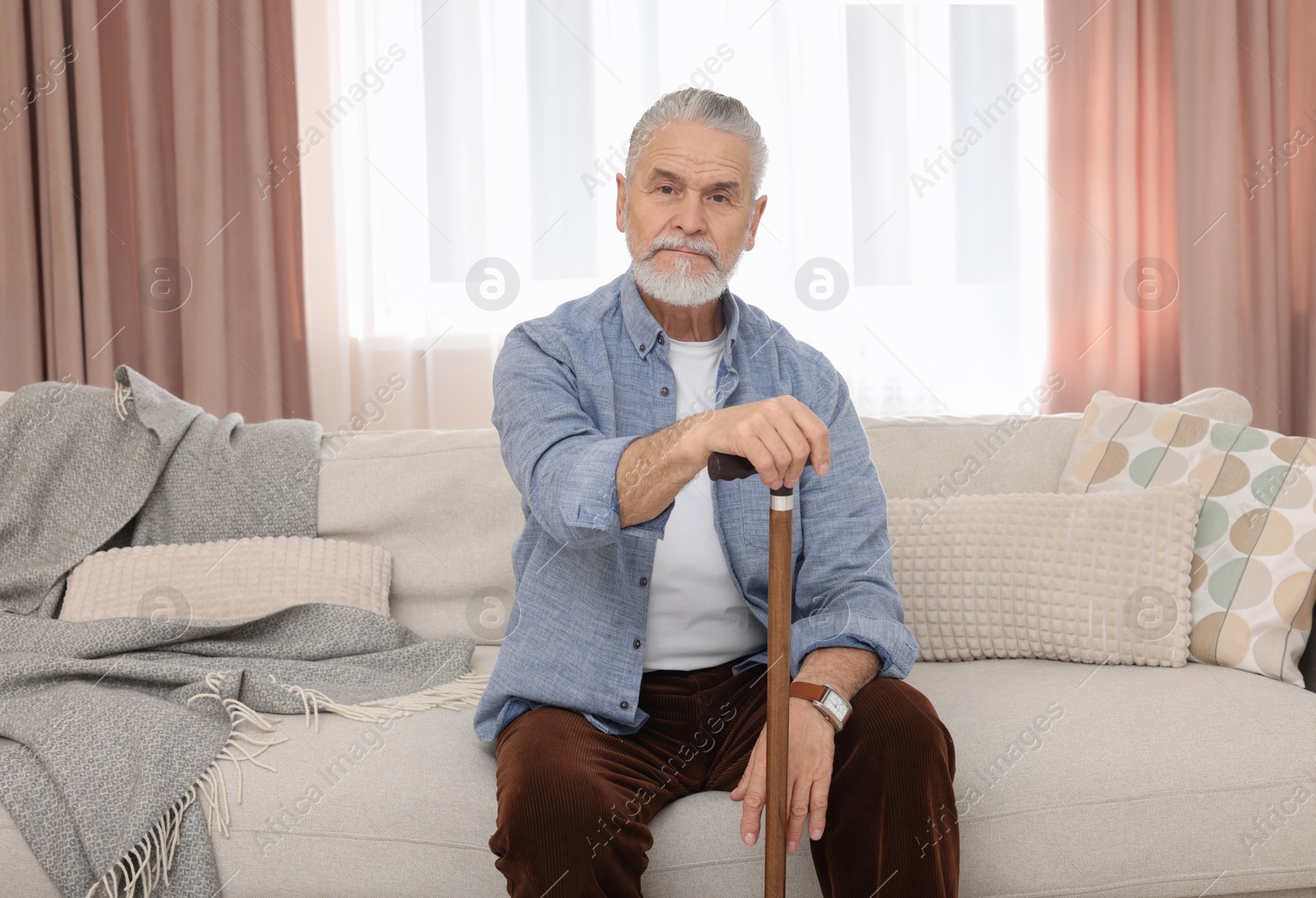 Photo of Senior man with walking cane sitting on sofa at home