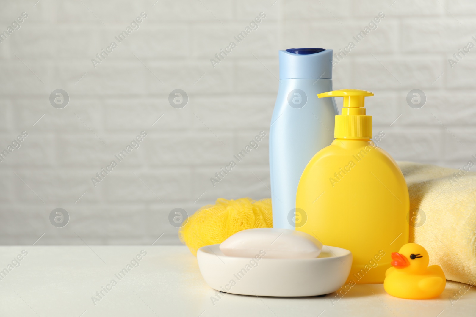 Photo of Baby cosmetic products, bath duck, sponge and towel on white table against brick wall. Space for text