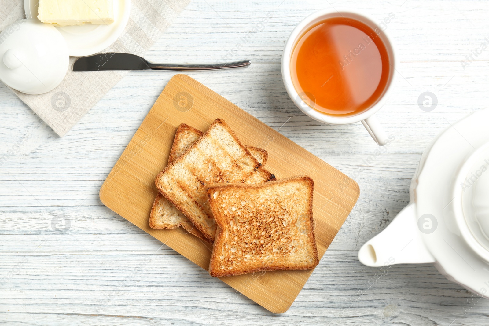 Photo of Board with toasted bread and cup of tea on wooden background, top view