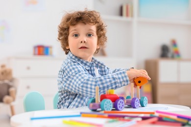 Cute little boy playing with wooden toys at white table in kindergarten