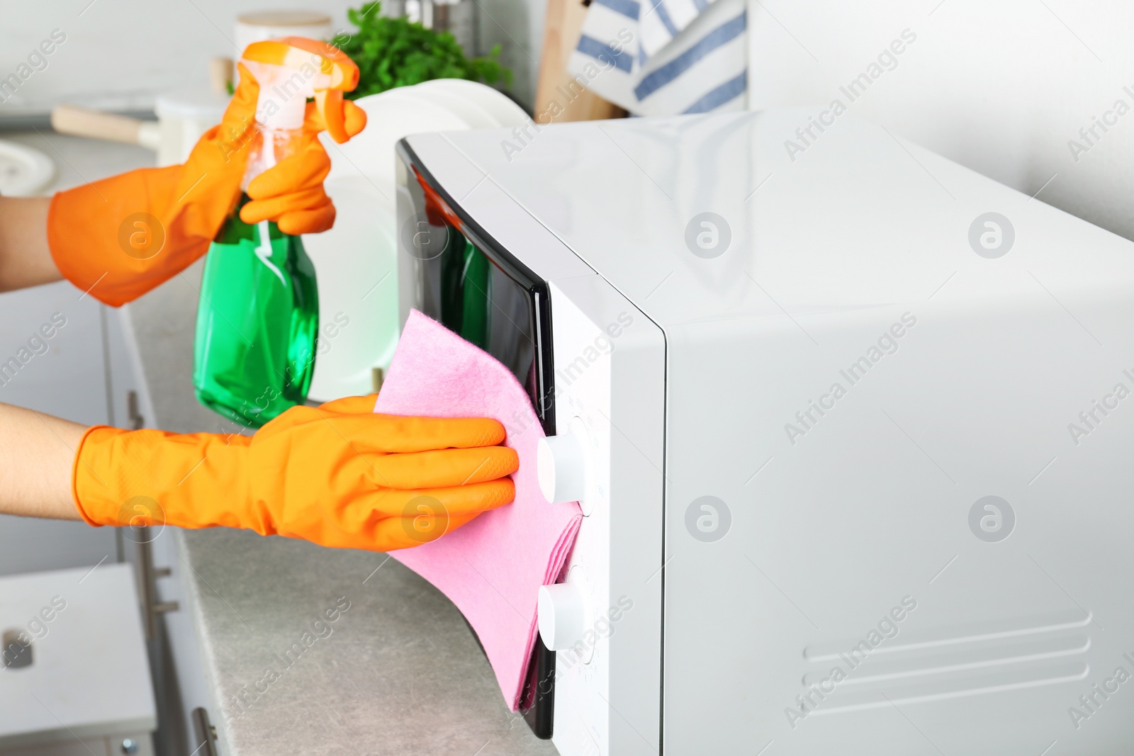 Photo of Woman cleaning microwave oven with rag and detergent in kitchen, closeup