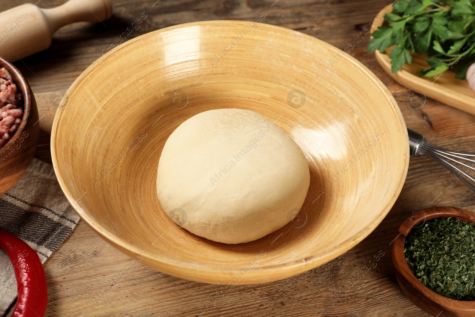 Photo of Bowl with raw dough and products on wooden table, closeup