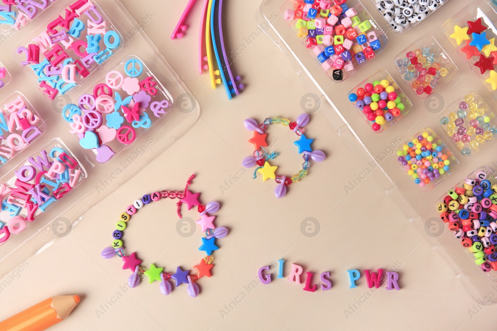 Photo of Handmade jewelry kit for kids. Colorful beads, wristbands and bracelets on beige background, flat lay