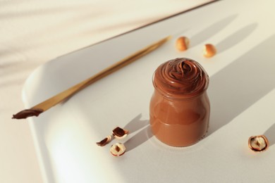 Glass jar with tasty chocolate hazelnut spread and nuts on white table