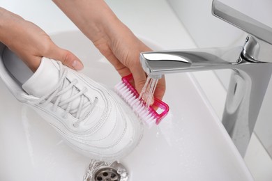 Woman washing shoe with brush under tap water in sink, closeup