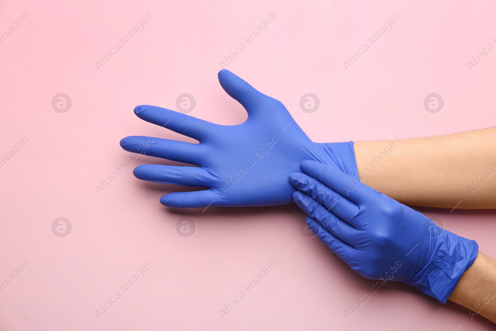 Photo of Person putting on medical gloves against pink background, closeup of hands