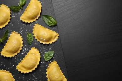 Photo of Raw ravioli with basil on black table, flat lay and space for text. Italian pasta