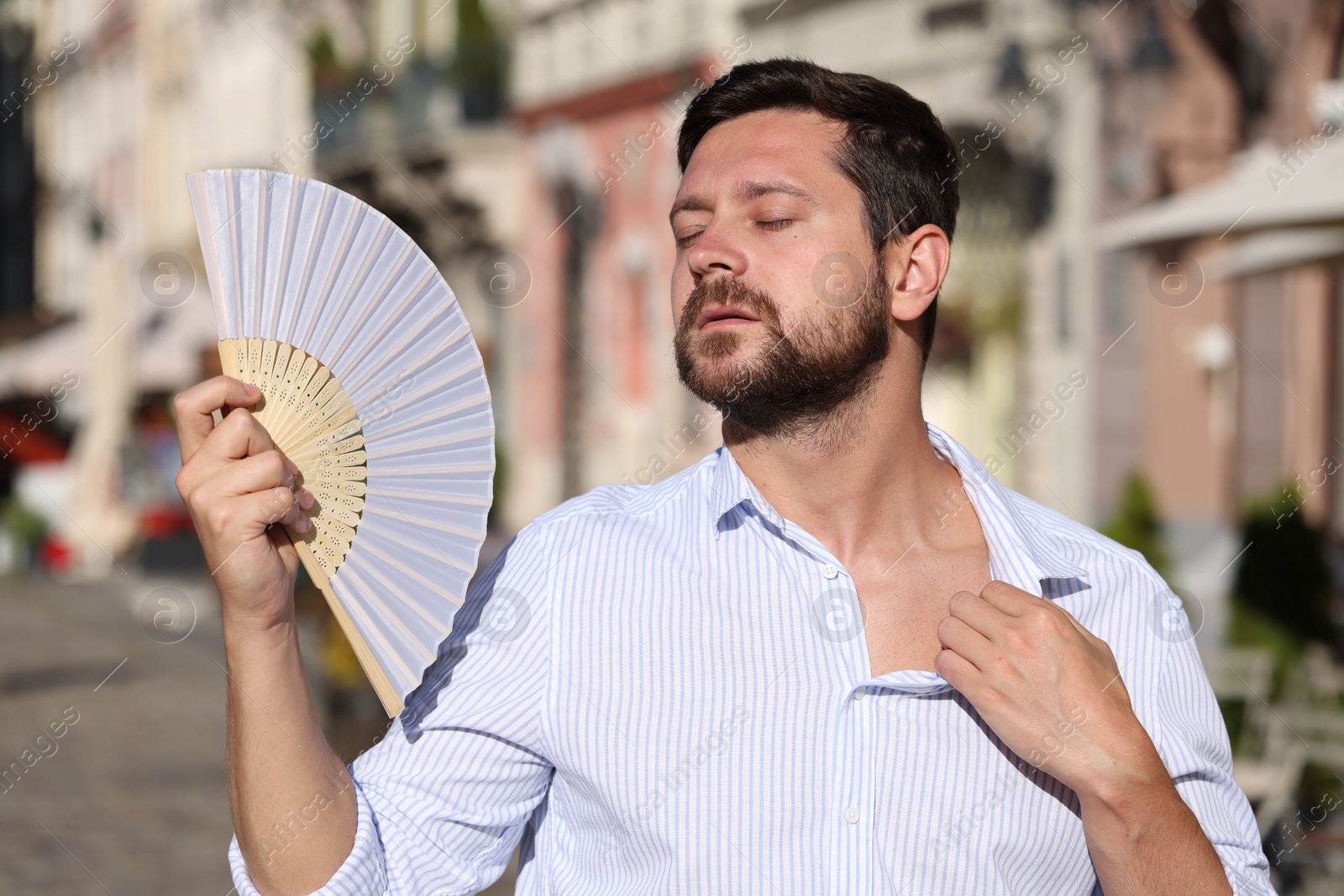 Photo of Man with hand fan suffering from heat outdoors