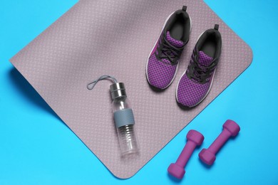 Photo of Exercise mat, dumbbells, bottle of water and shoes on turquoise background, flat lay