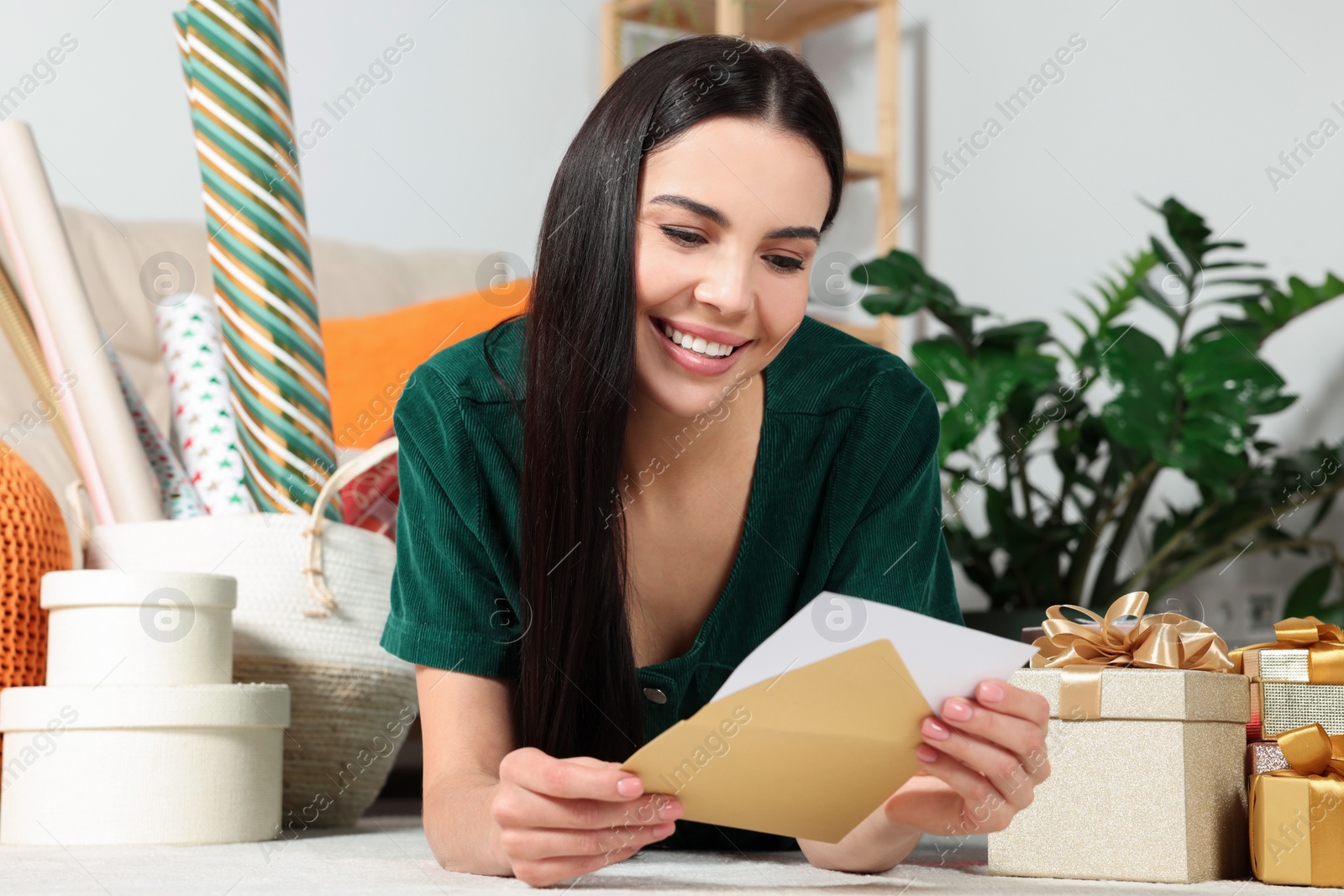 Photo of Happy woman reading greeting card on floor in living room