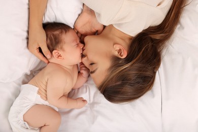 Photo of Mother kissing her cute newborn baby on bed, top view