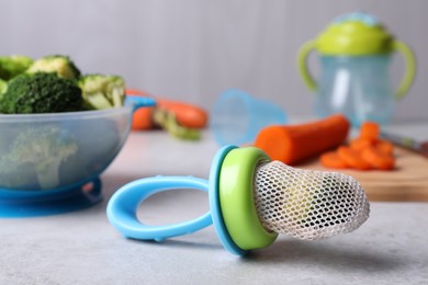 Photo of Nibbler with boiled broccoli on light grey table. Baby feeder