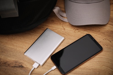 Smartphone charging with power bank, backpack and hat on wooden table