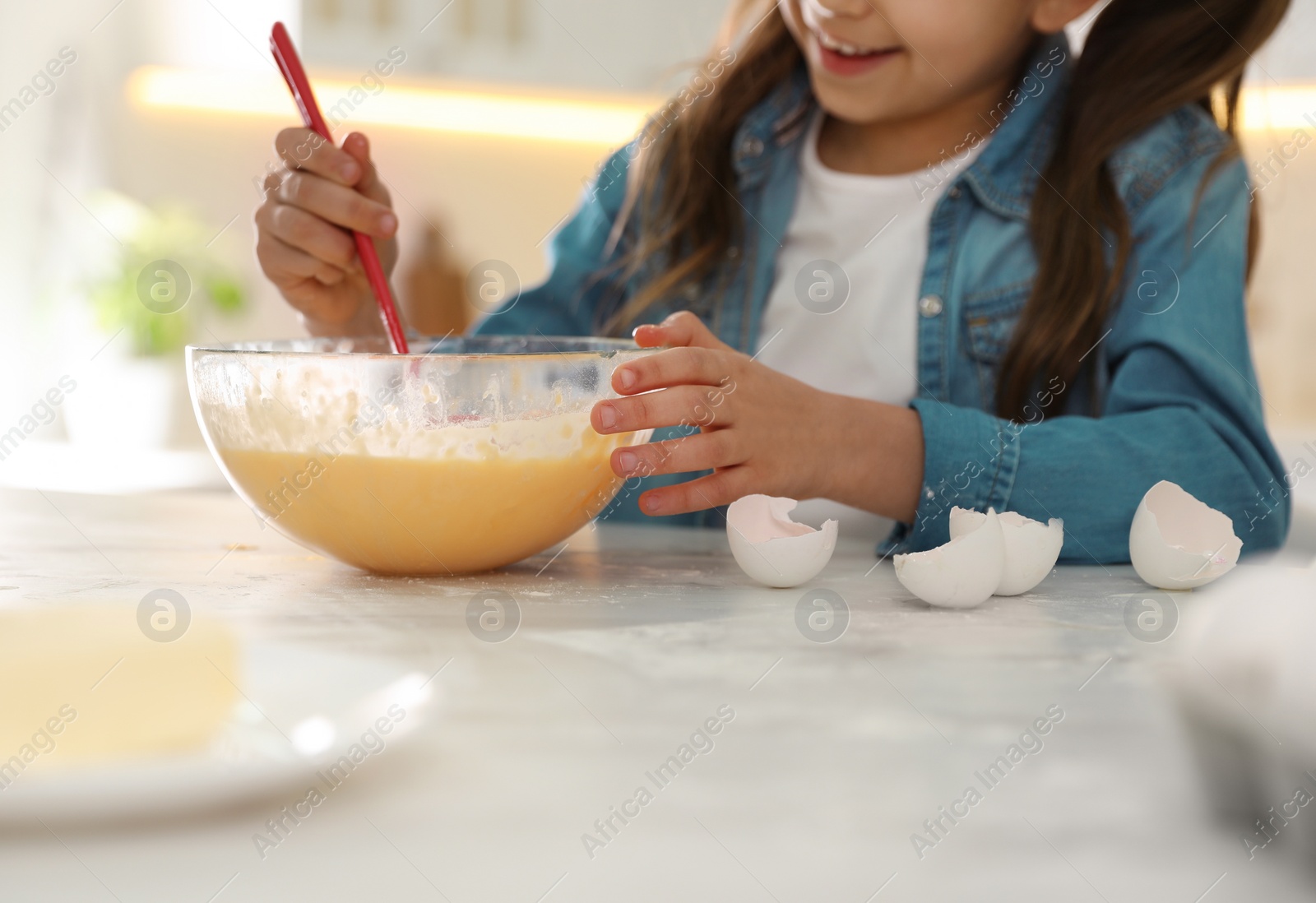 Photo of Cute little girl cooking dough at table in kitchen, closeup