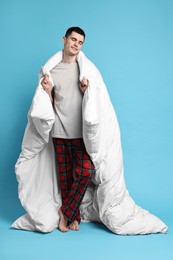Photo of Happy man in pyjama wrapped in blanket on light blue background